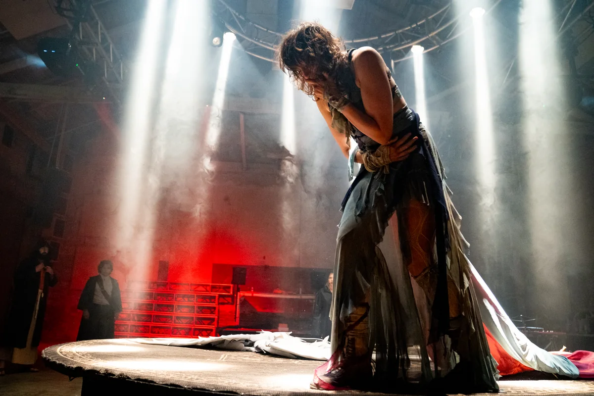 A performer bowed beneath shafts of stage light in The Golden Calf.